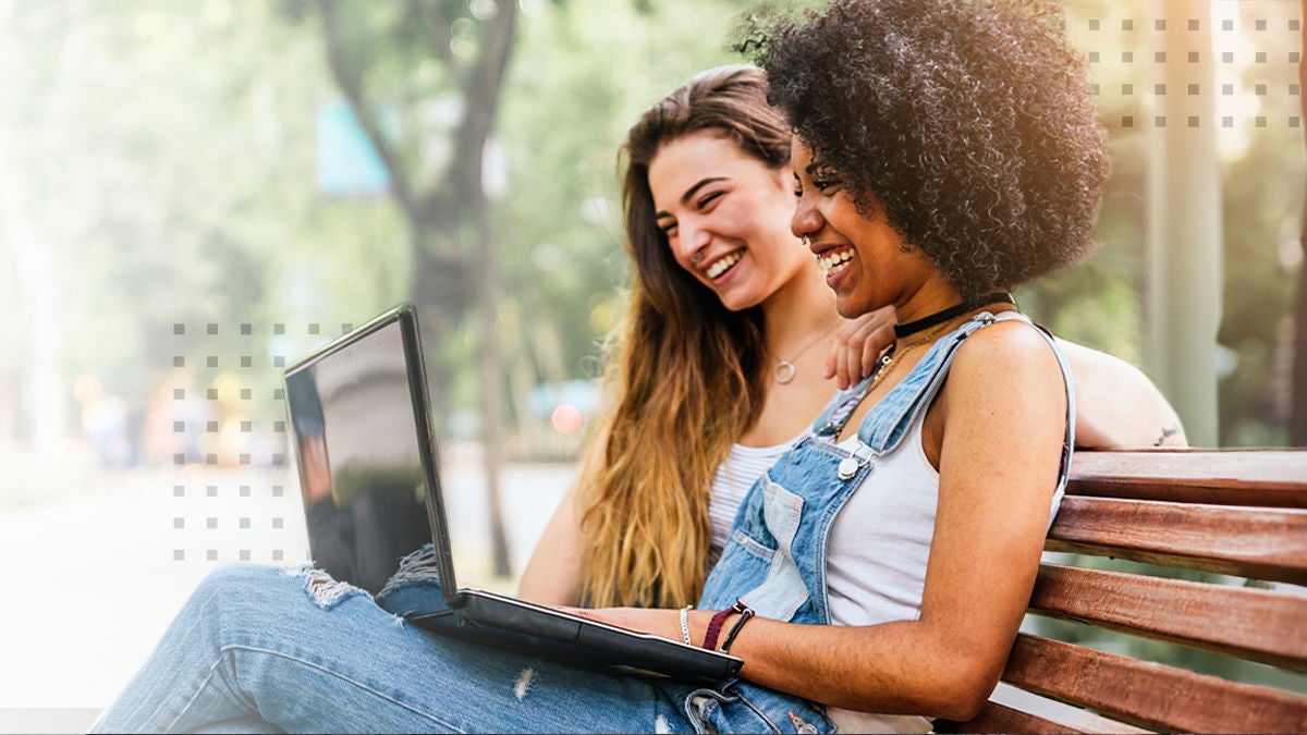 Two women smiling while using a laptop