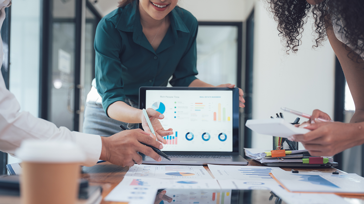 A woman presenting to a group using a display monitor showing business analytics