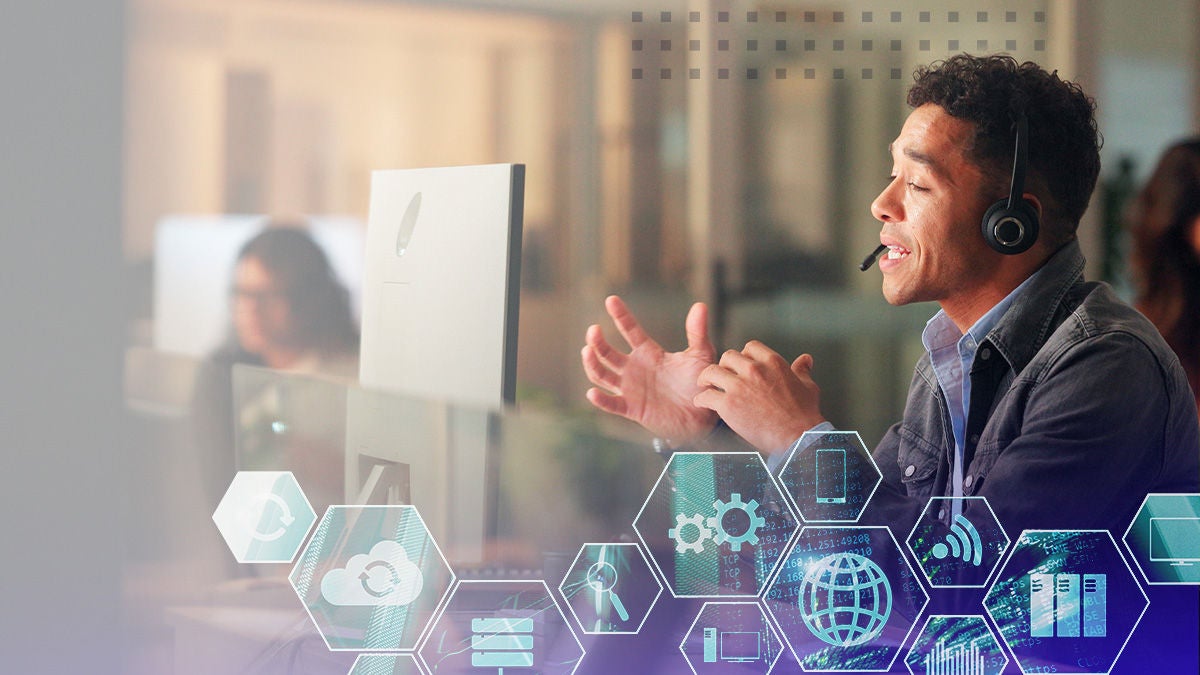 A man wearing a headset sits at a desk in a contemporary office environment, gesturing as he speaks. Digital hexagonal icons overlay the foreground, representing cloud computing, data, and connectivity. The scene features muted tones and a professional, collaborative mood, with another person visible in the background.