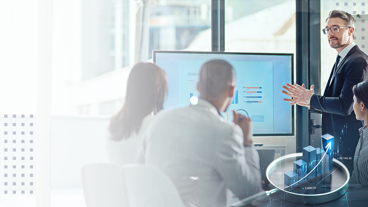 A group of employees sitting in a conference room with a coworker presenting business data on a large screen