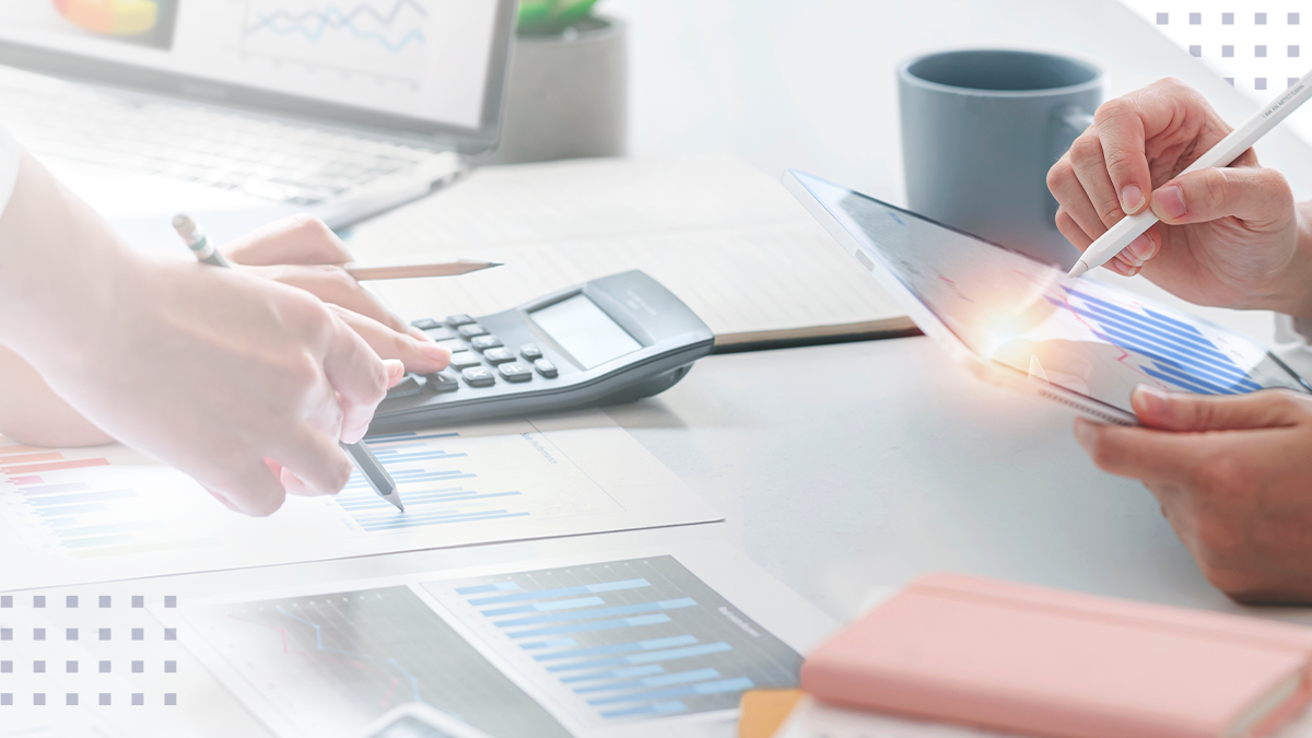 Coworkers at a table using tablets and a calculator while viewing business analytics