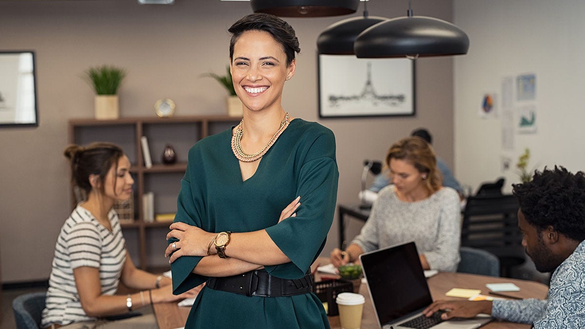 A woman smiling while standing during a meeting with coworkers around a table