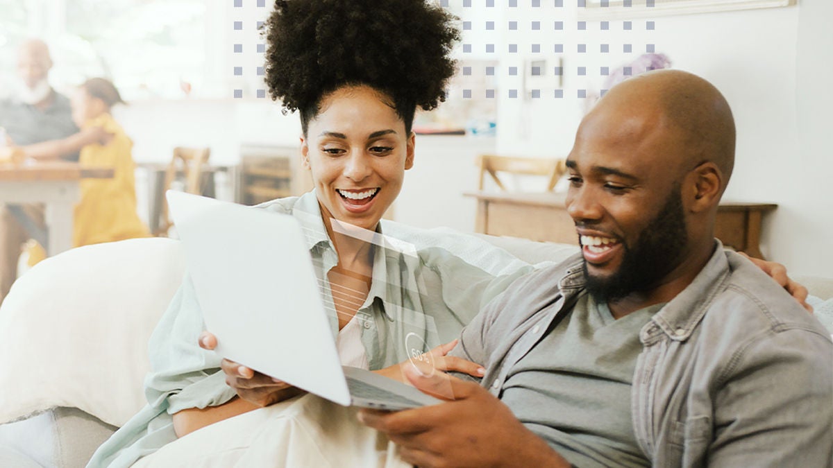 two smiling people sitting on the couch with a laptop