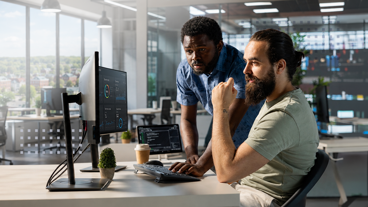 Two colleagues are working together at a desktop computer in a contemporary open-plan office