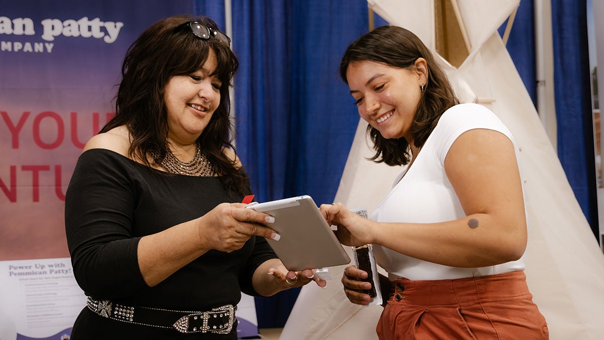Two woman looking at a tablet at a tribal community event
