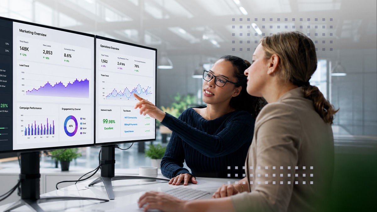 Two business professionals sit at a workstation reviewing analytics dashboards on dual monitors. One woman points at charts and graphs displaying performance metrics and data trends. The CalixOne and Fiber logos appear prominently at the top of the image, indicating a technology or telecommunications context. A blue banner labeled PRESS RELEASE overlays the bottom left, suggesting an official announcement or corporate communication.