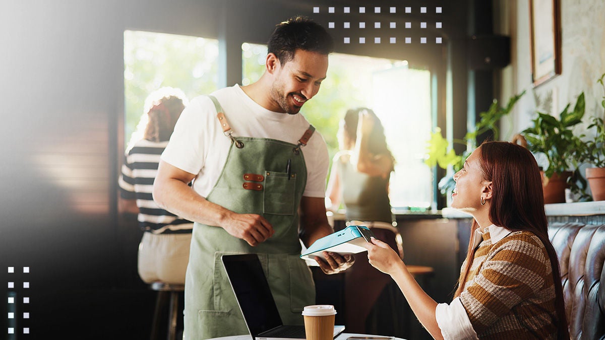 A barista wearing an apron holds a tablet toward a seated customer in a café. The woman reaches out to interact with the device while her laptop and a takeaway coffee cup sit on the table. Sunlight streams through large windows, creating a warm and welcoming atmosphere. Subtle graphic elements overlay the image, adding a modern, digital feel.