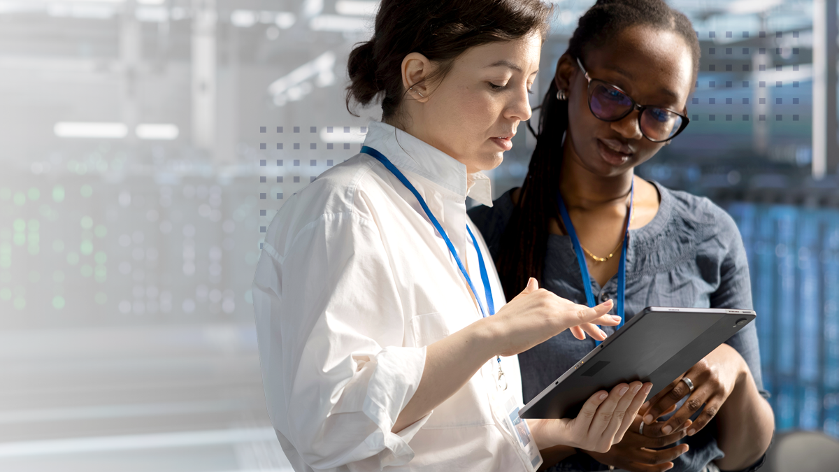 Two women are engaged in discussion while viewing a tablet device in a modern office environment