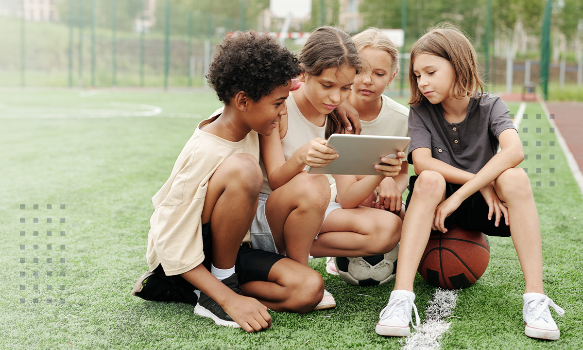 A group of children sitting on a grass field viewing a tablet