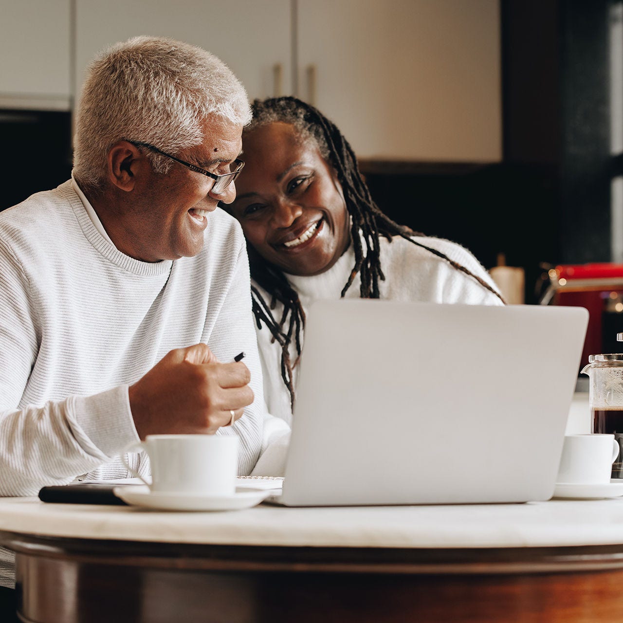 A smiling senior couple sitting at a table with coffee mugs and a laptop