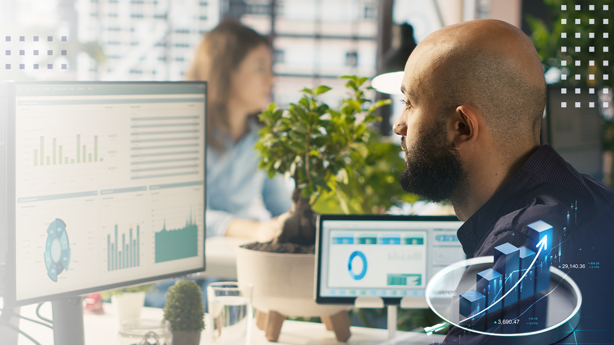 A man in an office using a computer with analytics and data displayed with graphs on the monitor