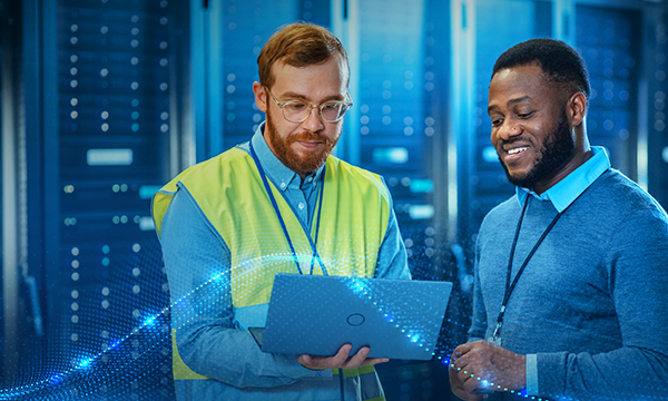 IT specialist in glasses with a laptop discussing with technician Colleague in data center while standing next to server racks