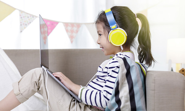 Asian little child girl learning at home wear headphone talk video calling with laptop meeting online app